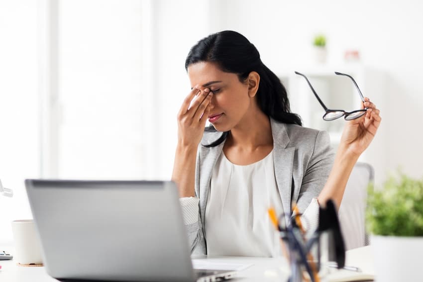 Mujer en la oficina con los ojos cansados, sosteniendo sus lentes tras mucho tiempo frente a la pantalla