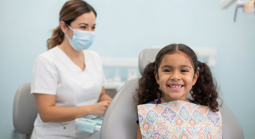 Niña sonriendo en el sillón dental, tranquila, con la odontopediatra a su lado